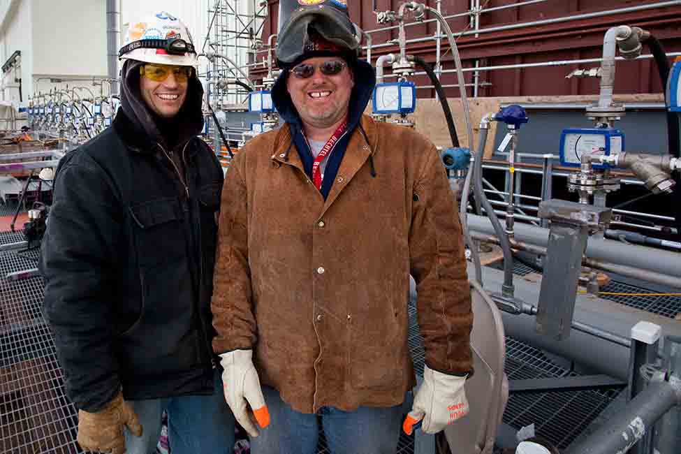 Two craft workers smiling in front of construction site. 