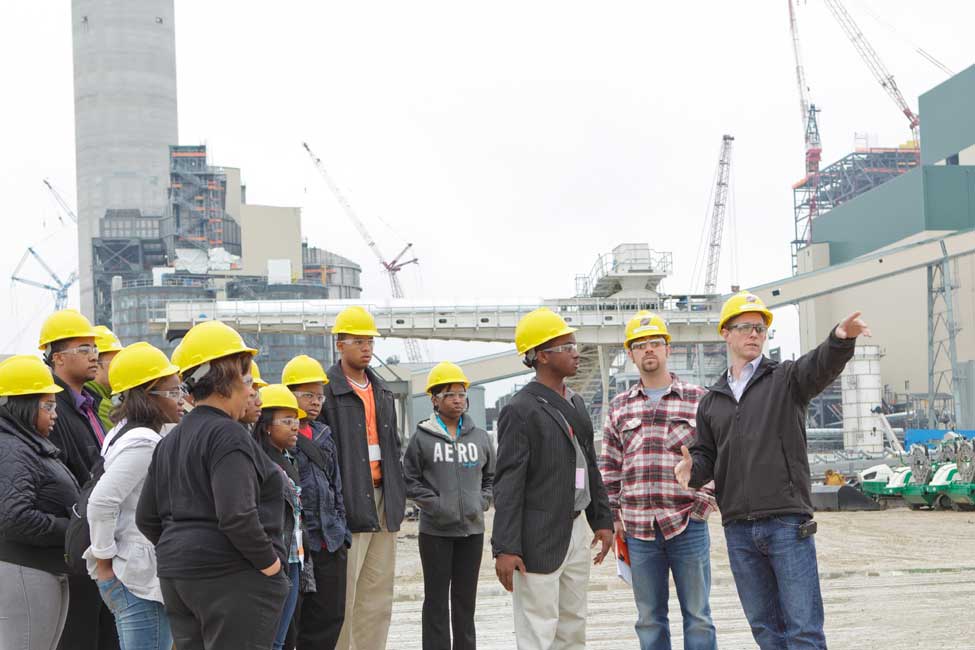 a group of students in hard hats on a tour at a shipyard