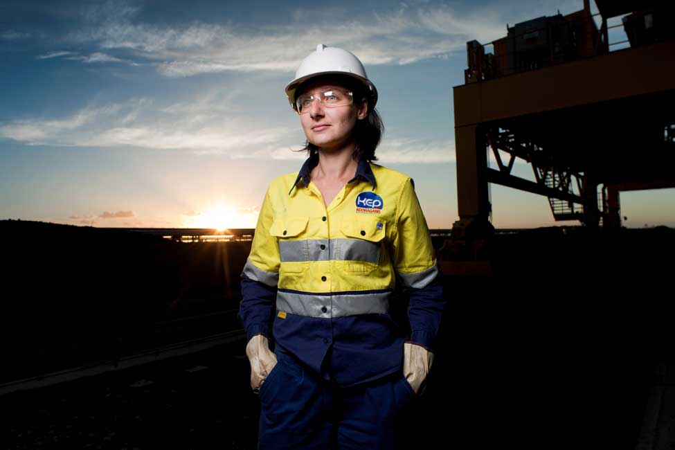 Female Bechtel colleague standing in front of coal plant looking off to the left. 