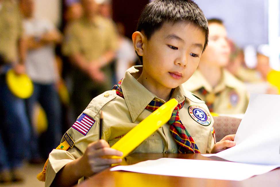 a boy in a cub scout uniform works at a desk