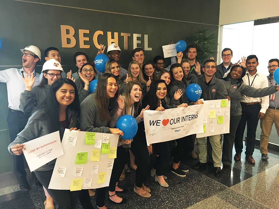 Group of young men and women holding I love Bechtel sign in lobby of building