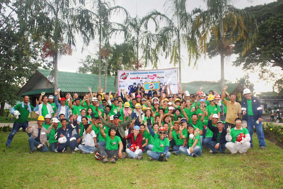 A large group of volunteers in matching green shirts pose in front of a Bechtel sponsored charity construction project