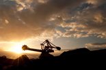 Silhouette of excavator with sun peaking over hills creating light flares