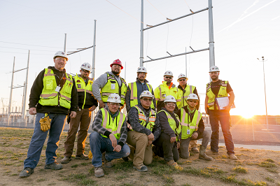 eleven workers pose in front of a transformer yard