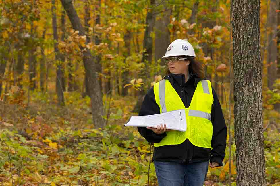 Women in hardhat and vest holding a pamphlet while standing near trees