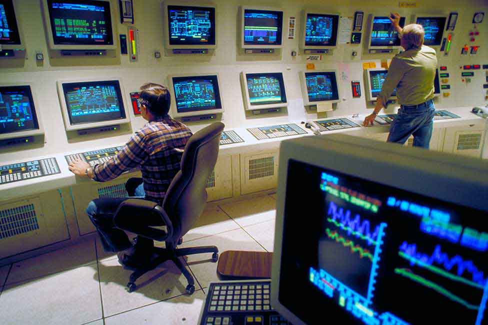 Computer control room with two men monitoring all the screens. 