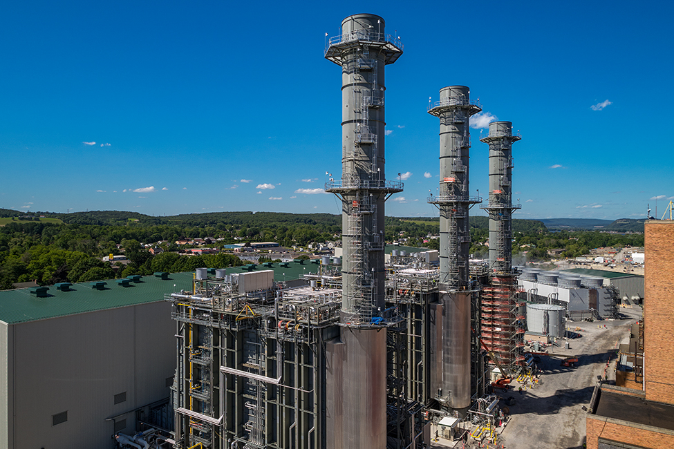Combined Cycle power plant in front of green hills and blue sky.