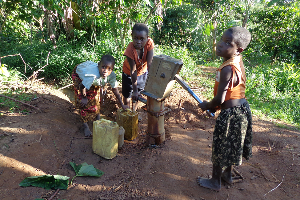 three young children fill up water jugs at a hand-operated pump