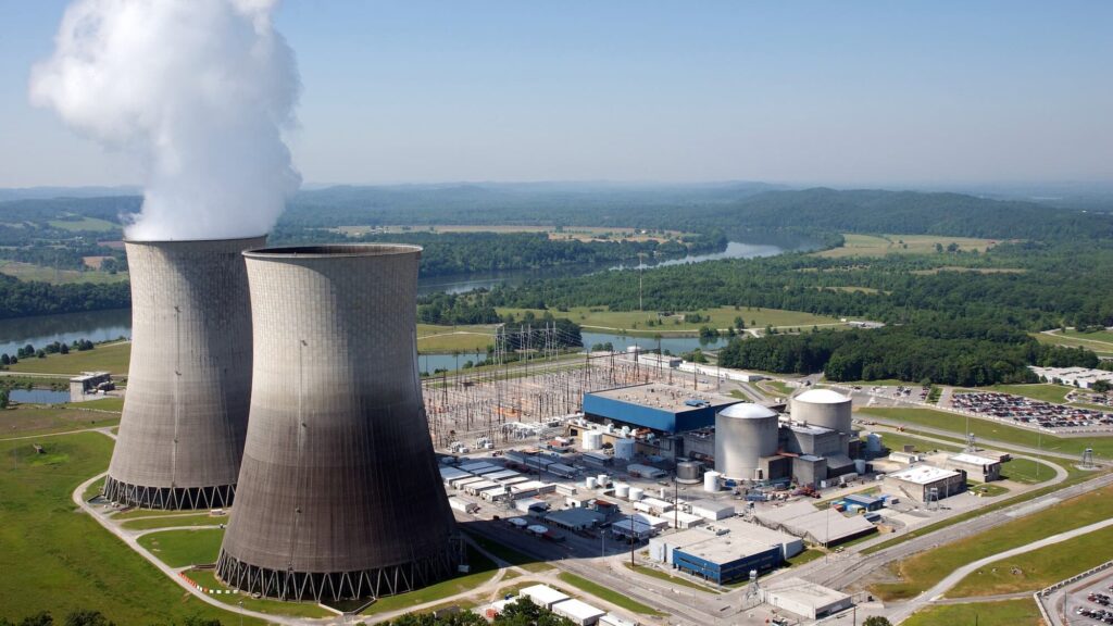 Exterior view of nuclear cooling silos against a blue sky with mountains and a river in the background