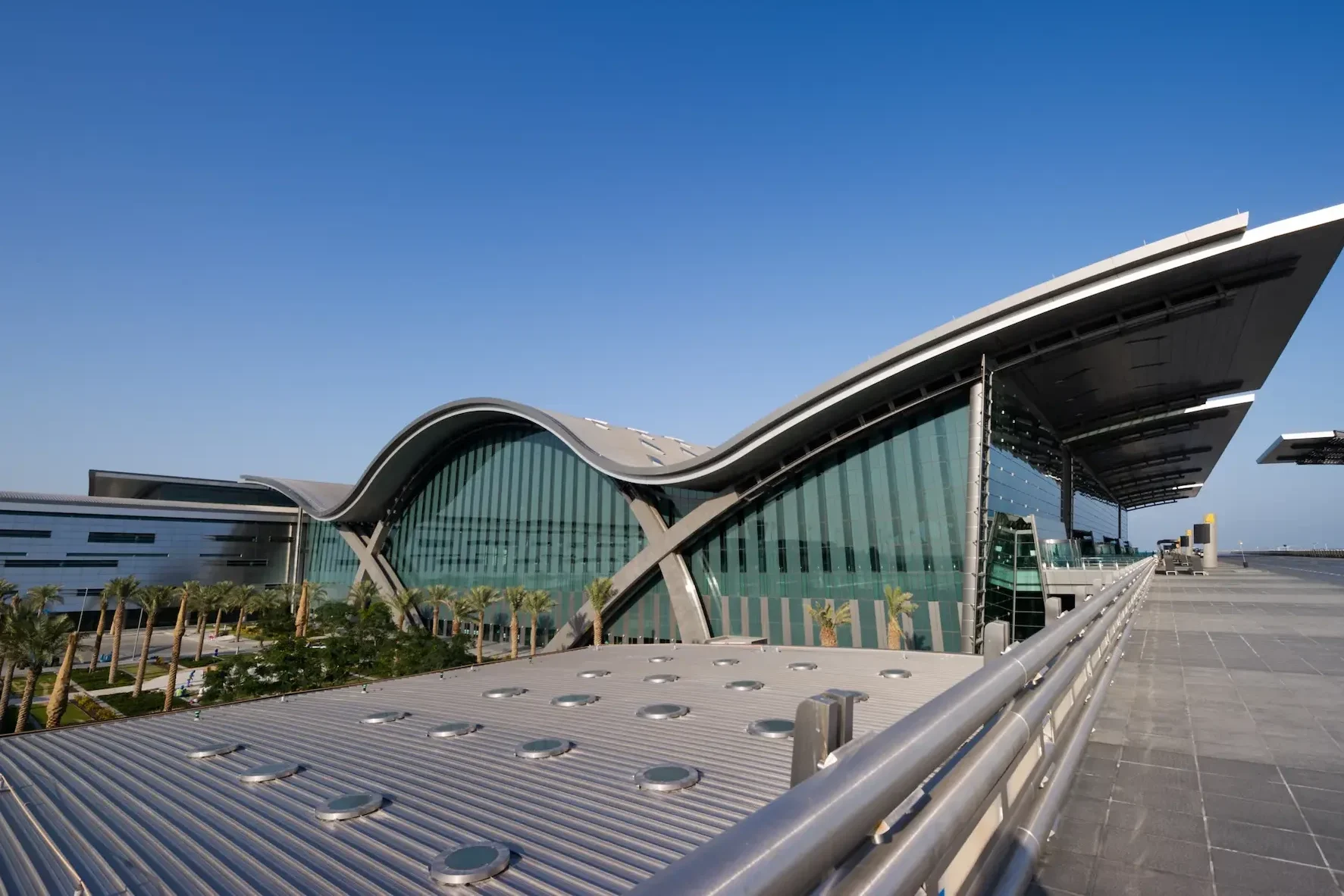 Exterior view of a modern airport with glass window walls and a wave shaped roof