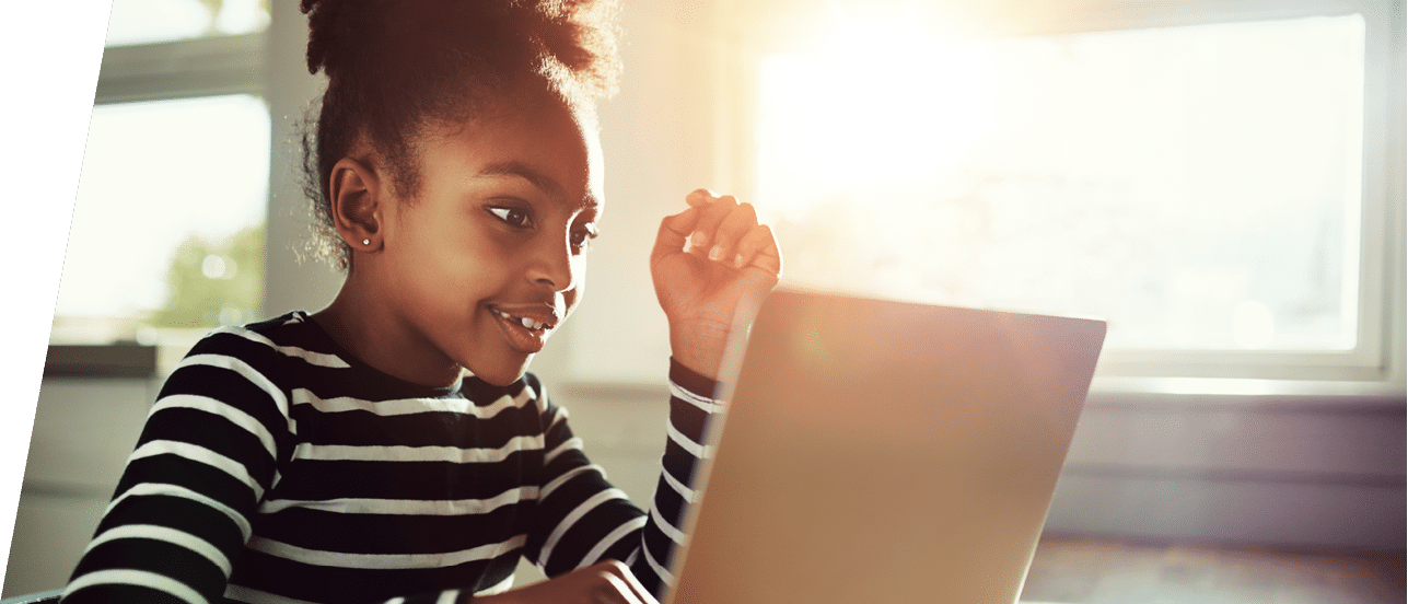 little ethnic girl sitting at home at a table working on her homework on a laptop computer reading the screen with a thoughtful expression